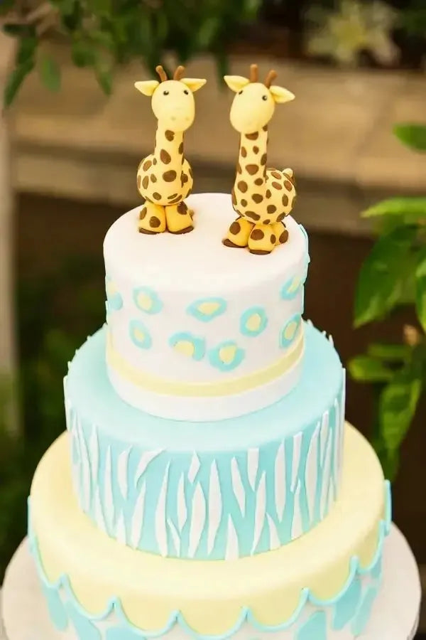 Animal-themed twins birthday cake with two giraffe toppers and pastel blue decorations