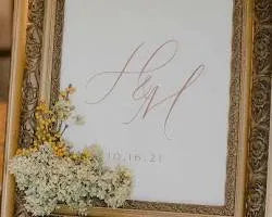 Elegant wedding sign with cursive initials in ornate gold frame and dried flowers