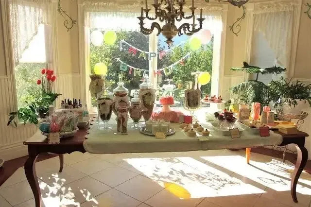 Breakfast birthday party table with pastries, treats, and 'Happy Birthday' banner in sunlit room