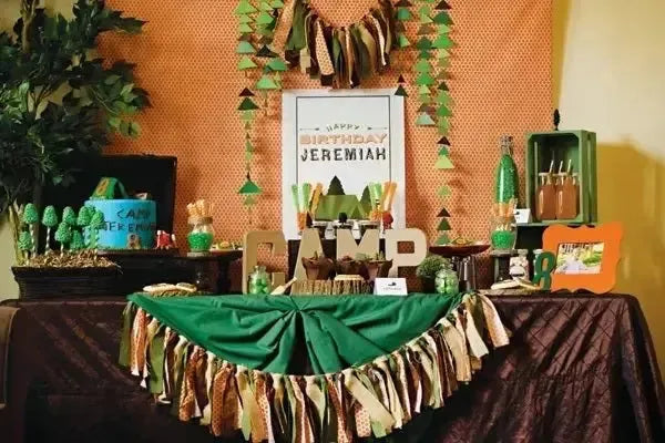 Camp-themed birthday party table with green, brown decorations and camping props