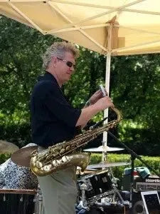 Saxophonist performing at outdoor wedding market under canopy, summer event band