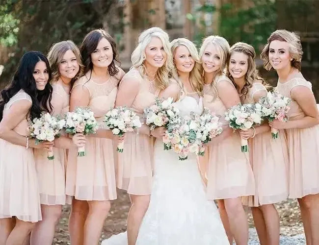 Bride with bridesmaids in blush dresses holding bouquets outdoors, wedding party photo
