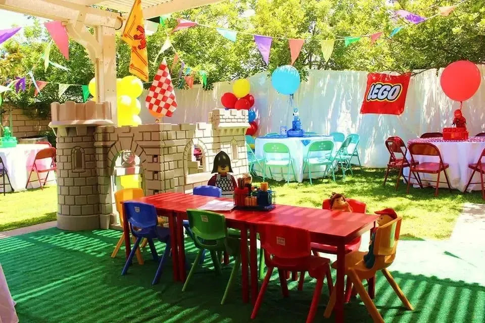 LEGO-themed birthday party with colorful tables, chairs, balloons, and castle decorations outdoors