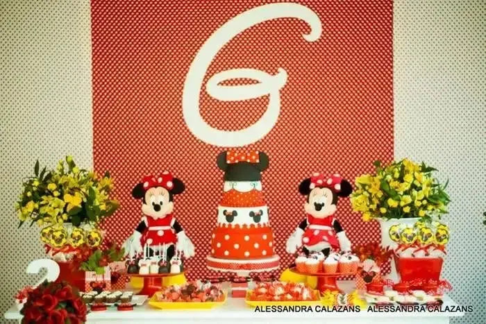 Minnie Mouse themed birthday dessert table with cake, plush toys, flowers, and red polka dots