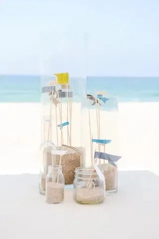 Nautical themed bridal shower table decor with sand jars and small sailboats by the beach