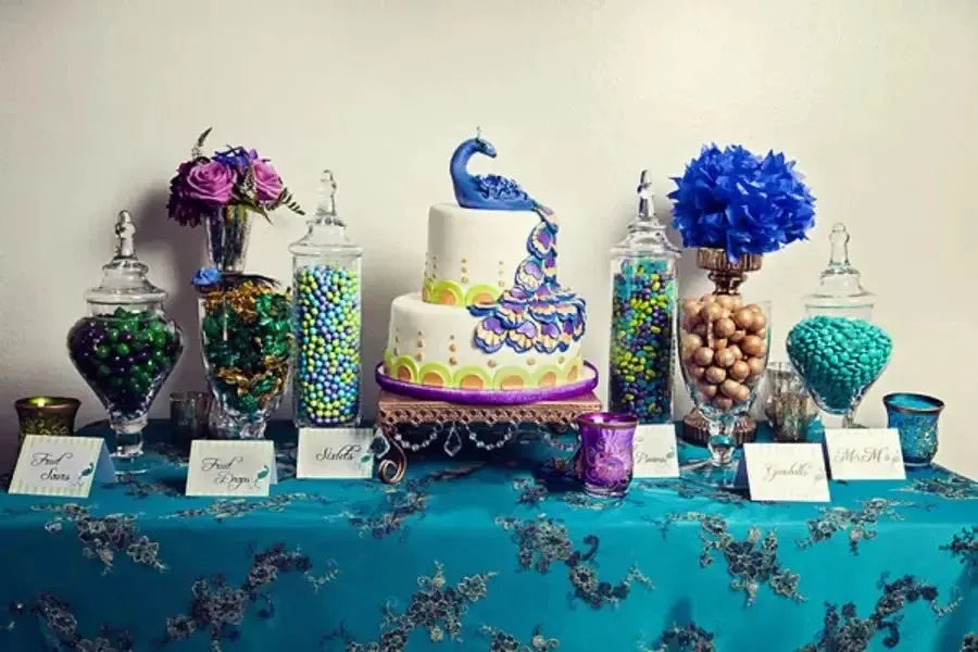 Peacock-themed baby shower dessert table with candy jars and a decorative peacock cake