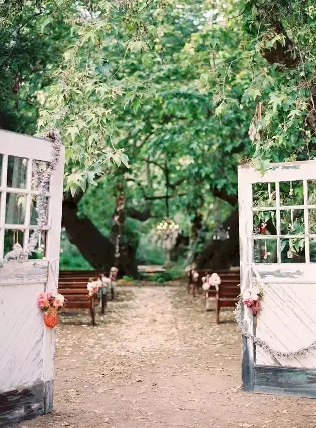 Rustic outdoor ranch wedding ceremony with vintage doors, floral decor, and wooden benches