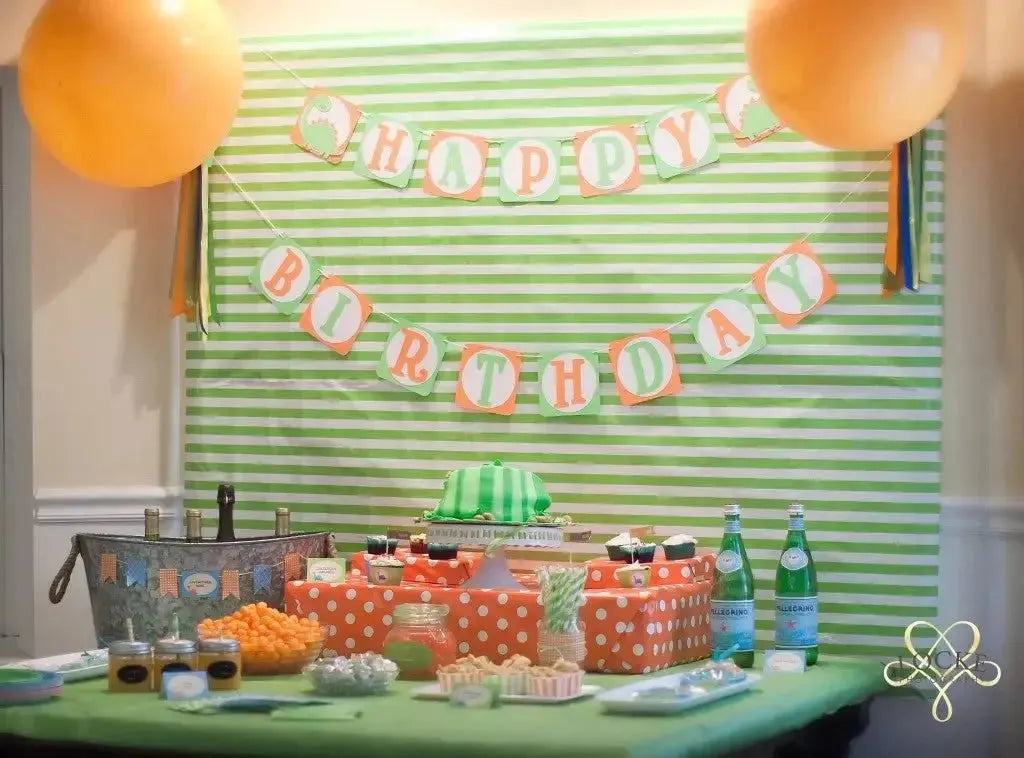 Dinosaur birthday party table with striped green backdrop, dino cake, balloons, and snacks