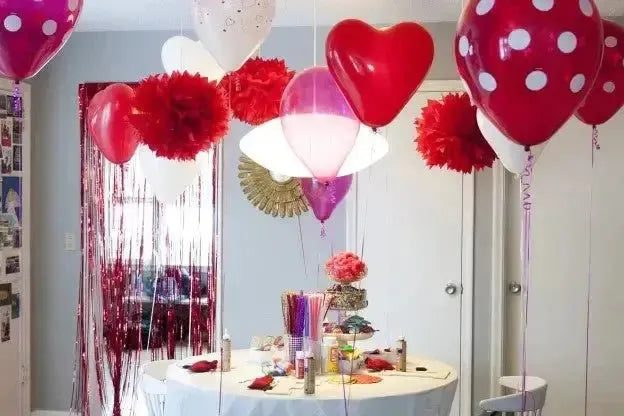 Valentine's Day party table with red heart balloons, pink decorations, and festive backdrop