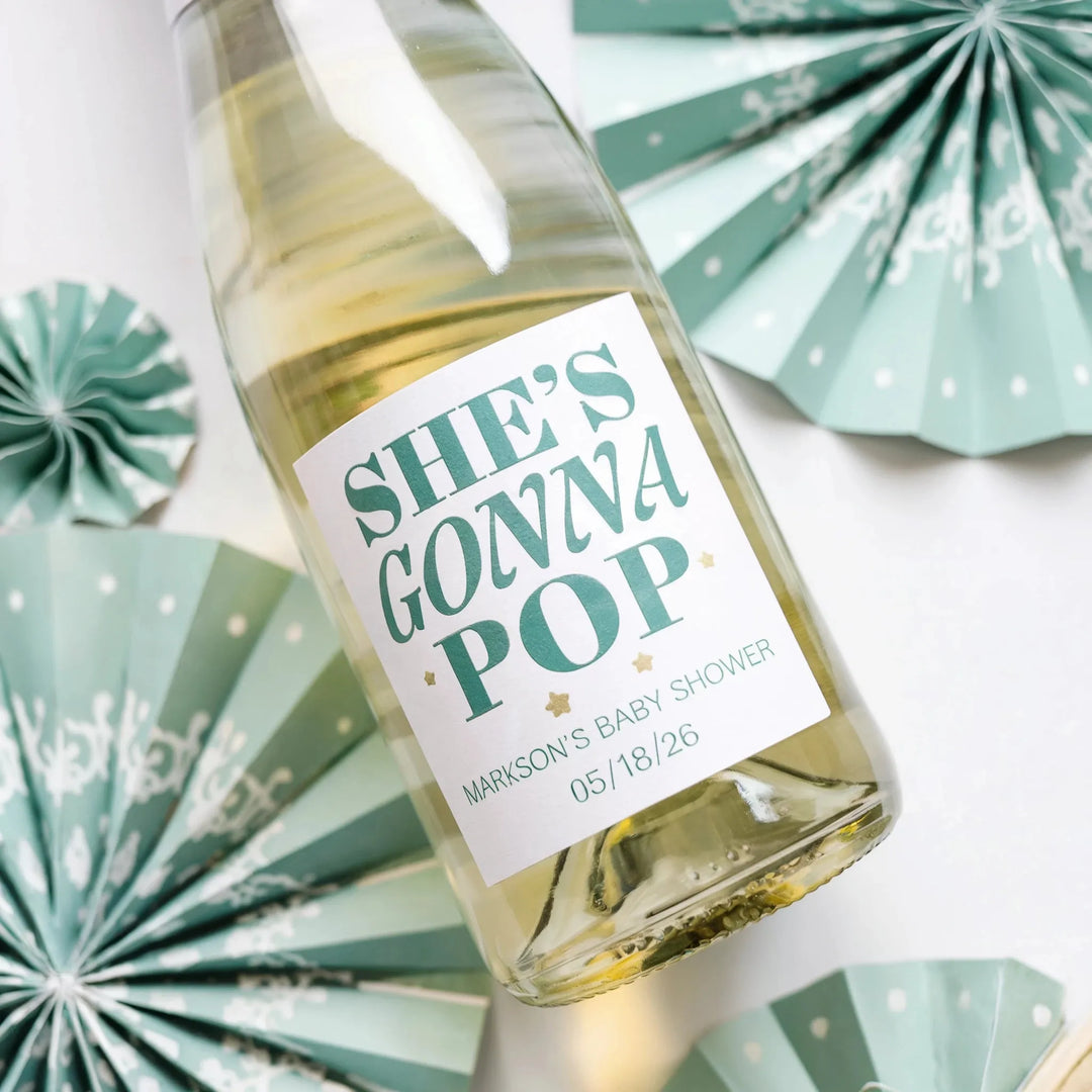 Custom baby shower champagne label on bottle with mint paper fans, festive party decor.