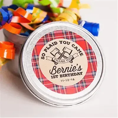 Round personalized birthday favor label with plaid design on a tin, surrounded by colorful ribbon.