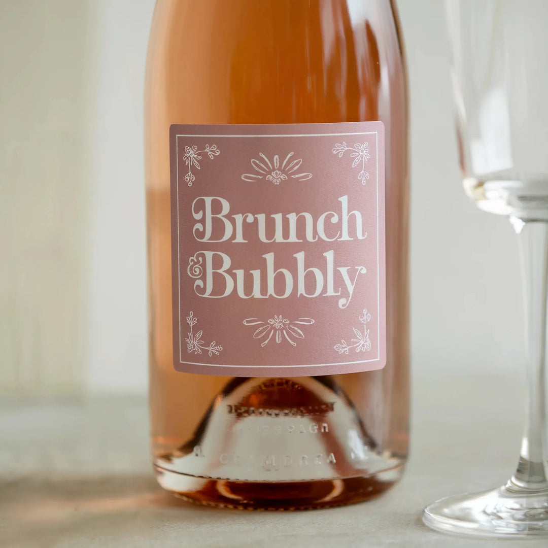 Custom pink champagne bottle label reading 'Brunch Bubbly' with floral design, beside glass
