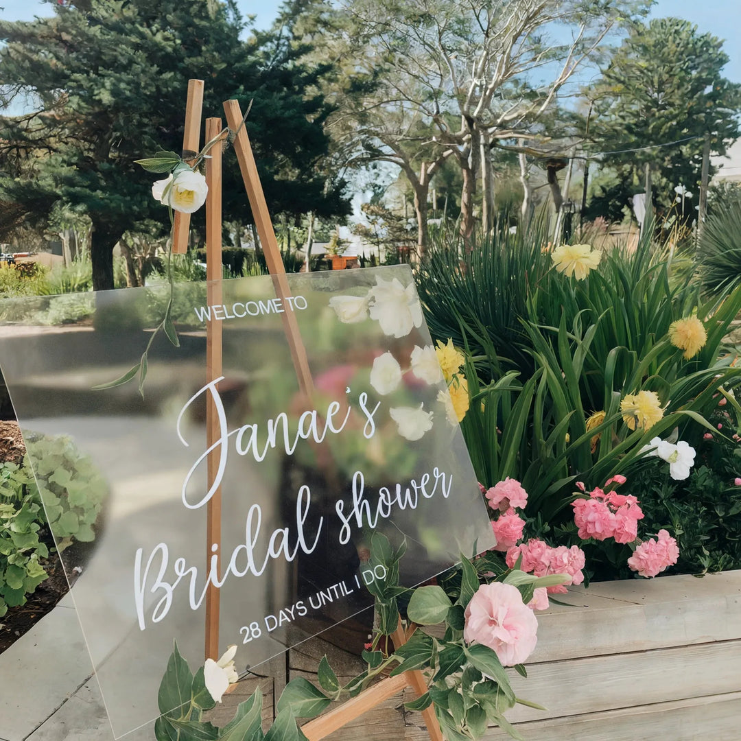 Custom bridal shower welcome sign with floral accents on easel in outdoor garden setting