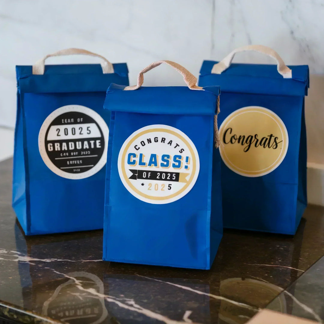 Blue party favor bags with custom graduation labels for class of 2025 on a marble table.