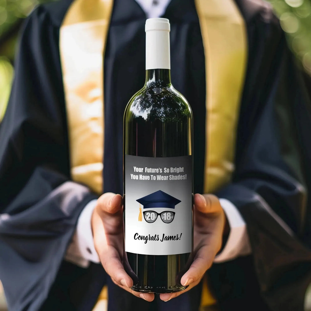 Person in graduation gown holding wine bottle with custom graduation label outdoors
