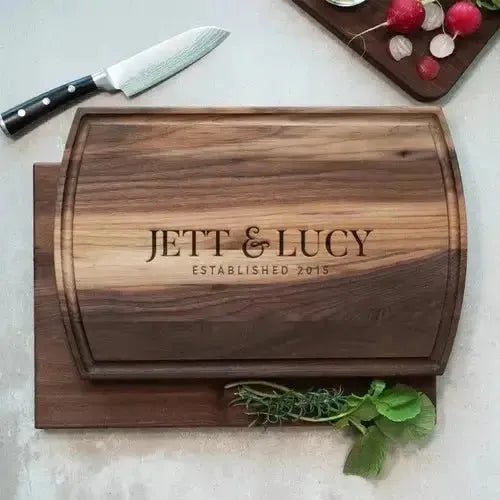 Personalized wooden cutting board engraved with 'Jett & Lucy Established 2015', kitchen herbs and knife nearby