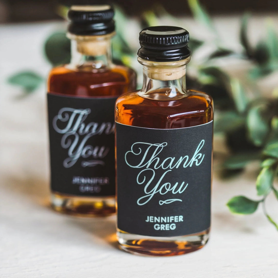 Wedding mini liquor bottles with personalized thank you labels on a white table