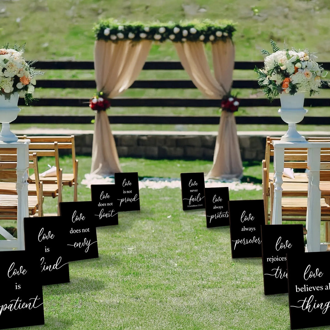 Outdoor wedding aisle with black 1 Corinthians 13 love quote signs and floral arch backdrop