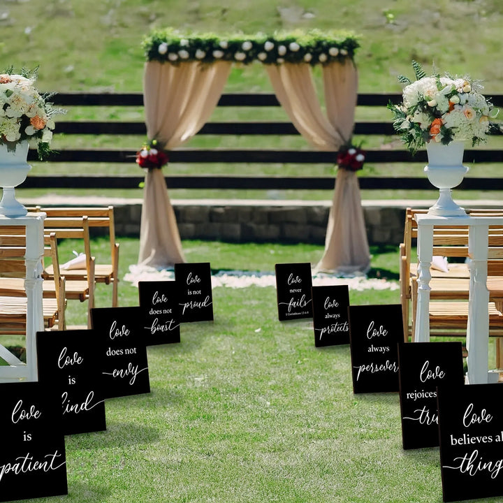 Outdoor wedding aisle with black 1 Corinthians 13 love quote signs and floral arch backdrop