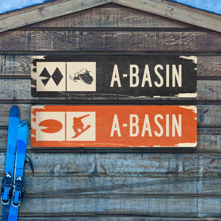 Distressed metal A-Basin ski trail signs with snowmobile and snowboard icons on wooden background