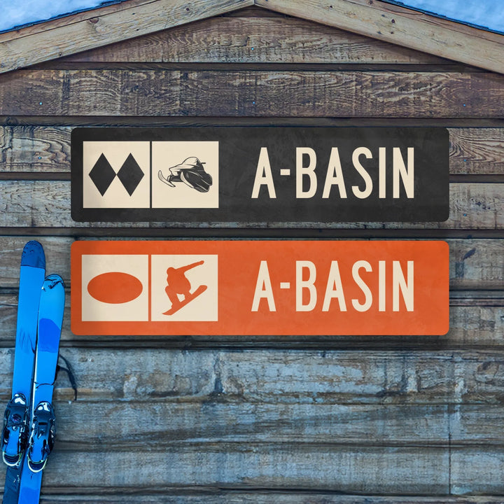 Two A-Basin ski trail metal signs mounted on rustic wood with blue skis leaning nearby