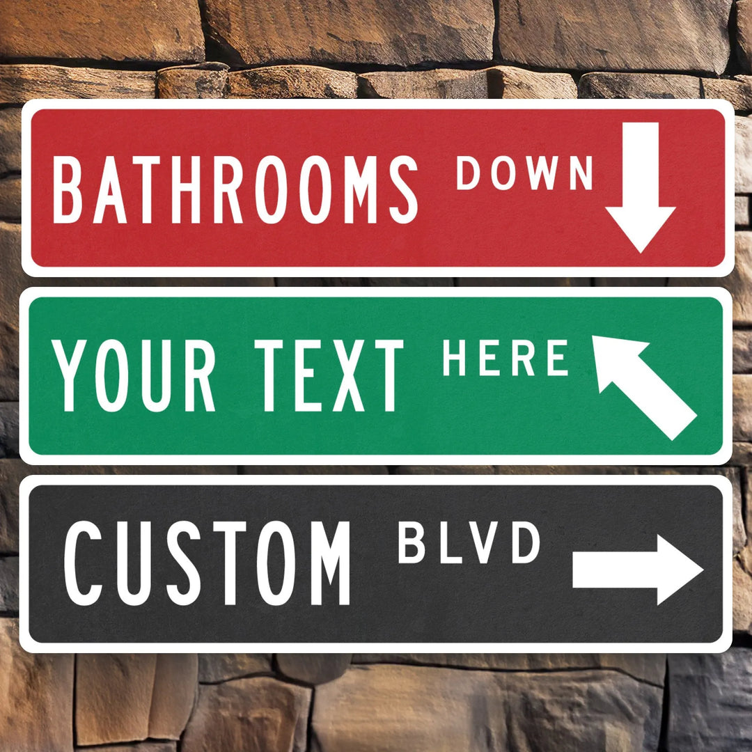 Three metal arrow street signs mounted on stone wall, red sign for bathrooms down, green customizable text sign, black custom boulevard sign
