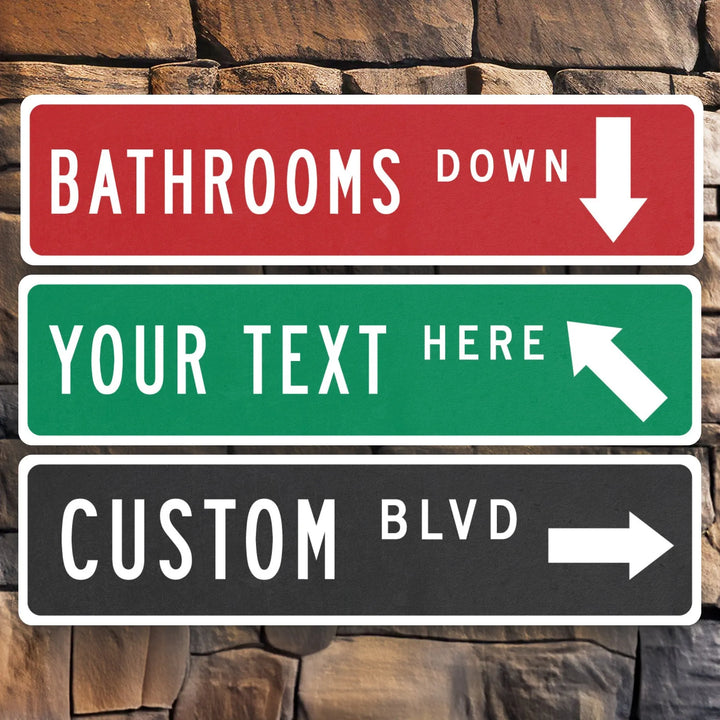Three metal arrow street signs mounted on stone wall, red sign for bathrooms down, green customizable text sign, black custom boulevard sign