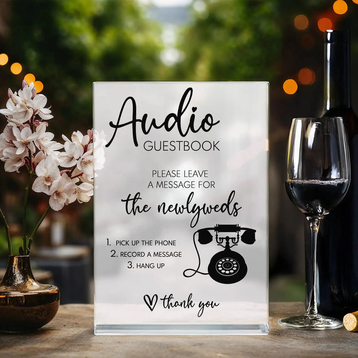 Wedding audio guestbook table sign with instructions next to flowers, wine bottle, and glass