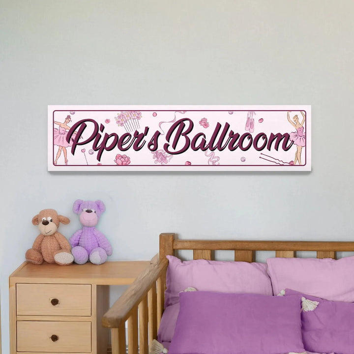 Pink wall sign reading Piper's Ballroom with ballerina and ballet-themed illustrations above a wooden bed with purple pillows
