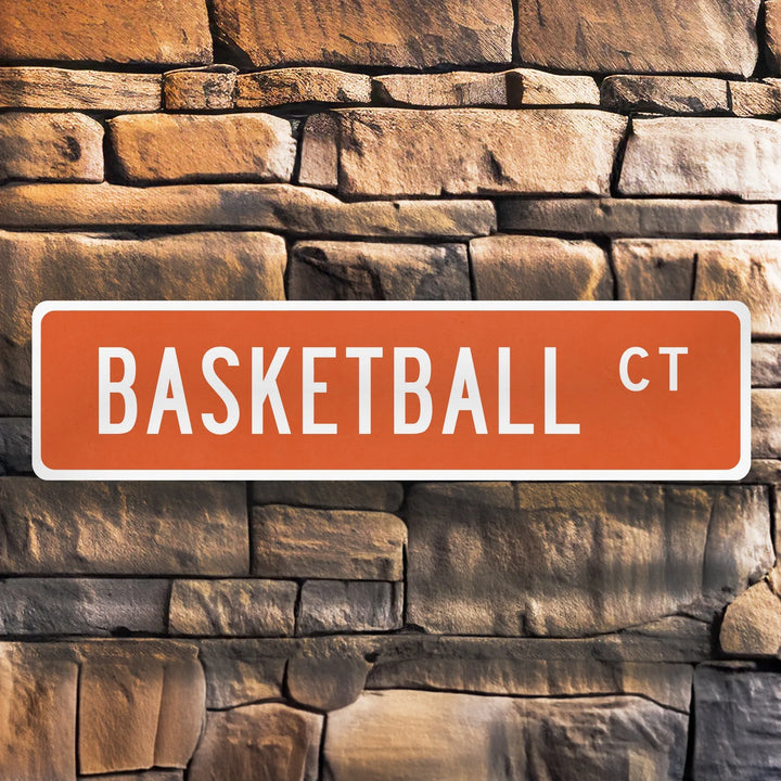 Orange metal street sign reading Basketball Ct mounted on textured stone wall