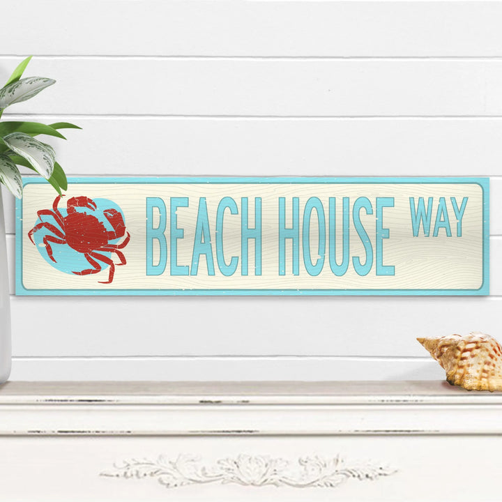 Beach House Way metal wall sign with red crab and light blue lettering on white wood background