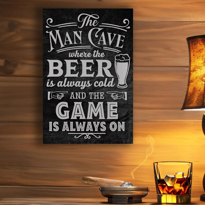 Black metal sign reading The Man Cave where the beer is always cold and the game is always on, with a lit cigar and glass of whiskey on wood wall