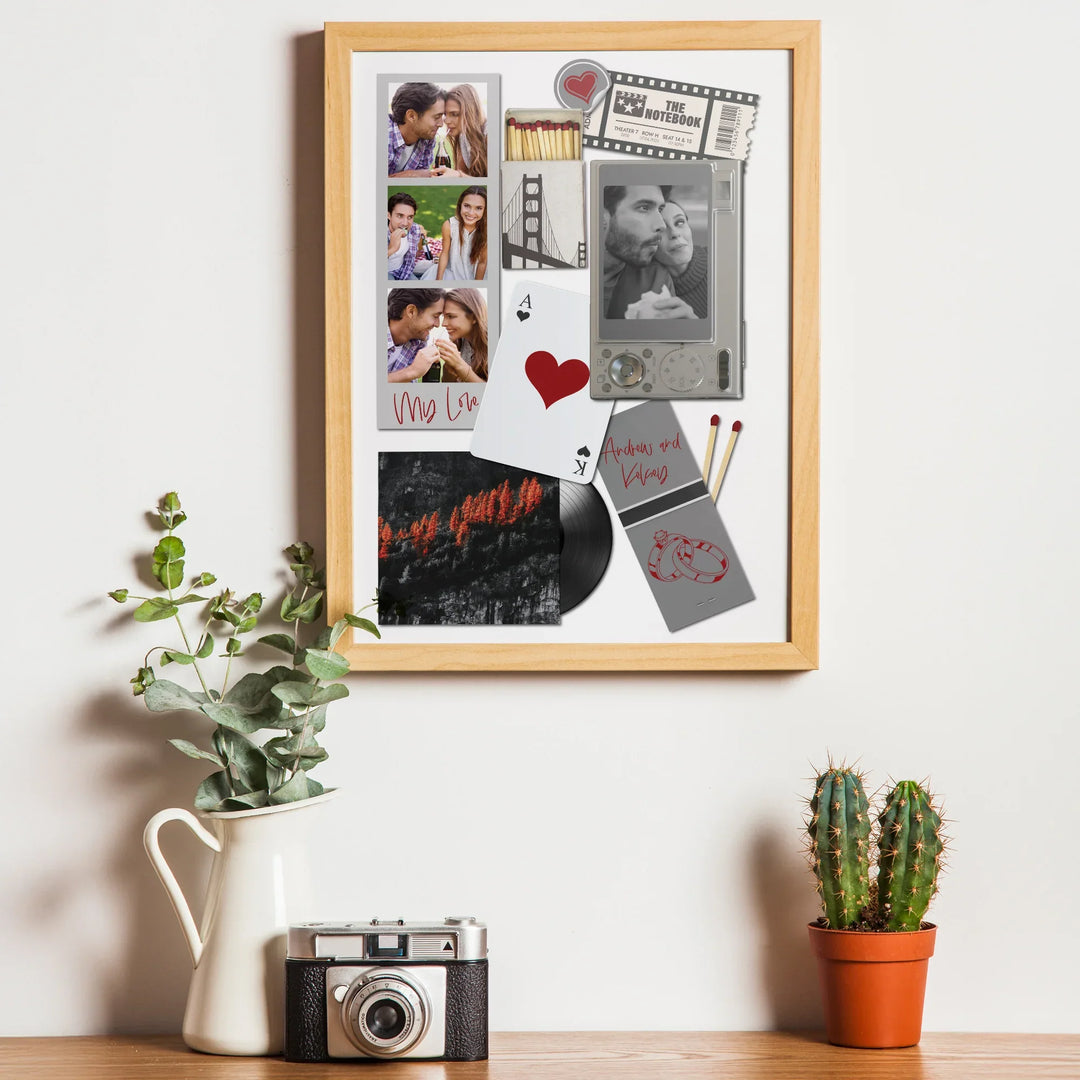 Framed collage of photos and memorabilia on a wall with a plant and camera on a table below.