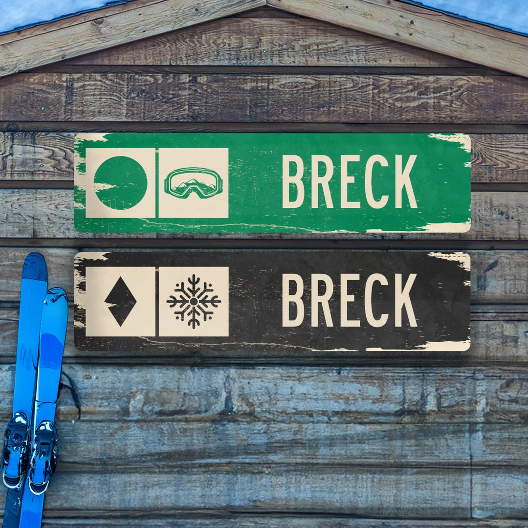 Distressed metal Breck ski trail signs with green circle and goggles, black diamond and snowflake, mounted on rustic wood