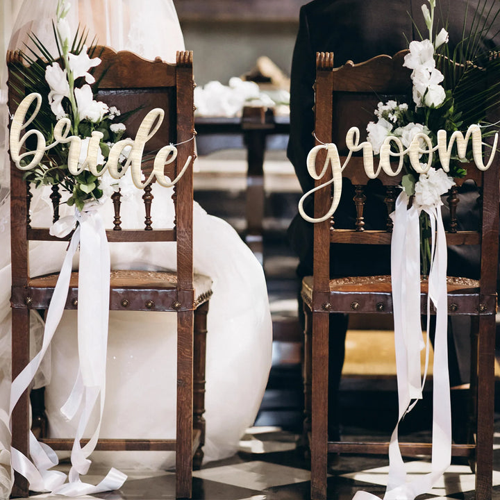 Wooden bride and groom chairs decorated with white flowers and ribbons at wedding ceremony