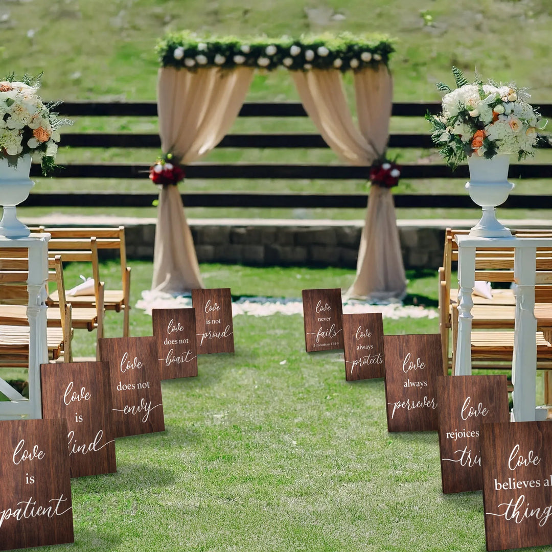 Outdoor wedding aisle with wooden Corinthian signs displaying love quotes and floral arch backdrop