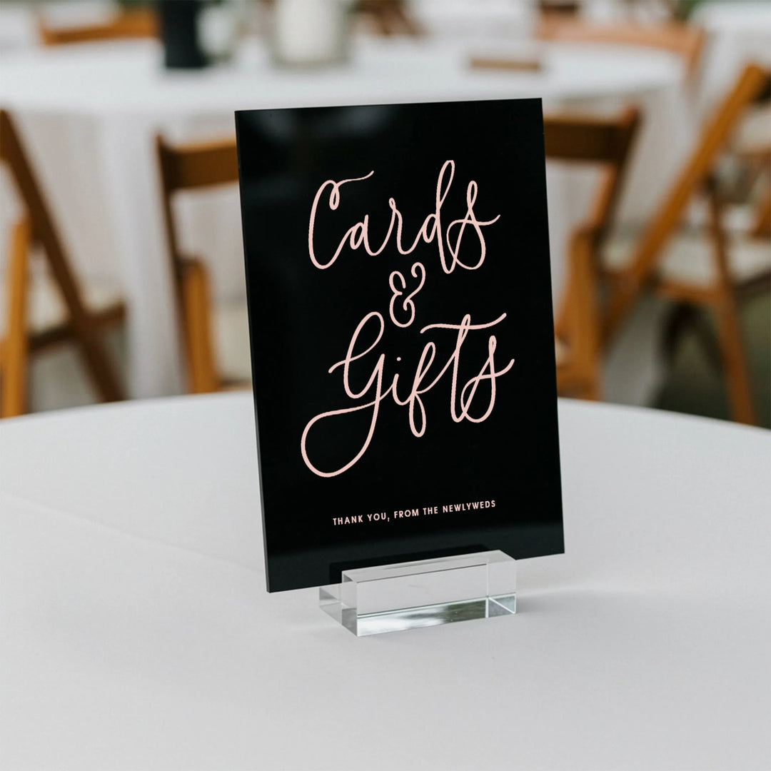 Black wedding cards and gifts sign with pink script on white table with wooden chairs