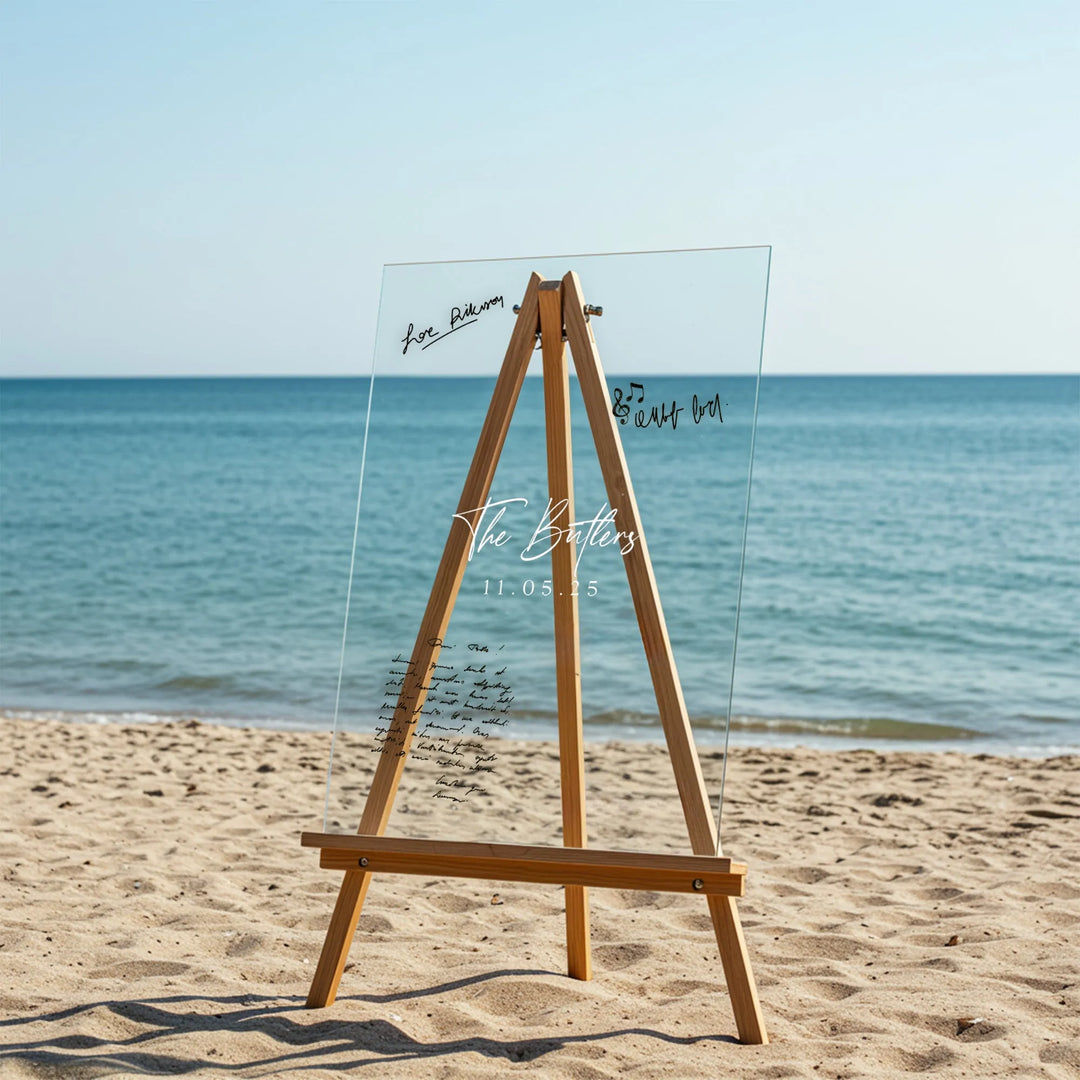 Clear acrylic wedding guest book on wooden easel with ocean and sandy beach background