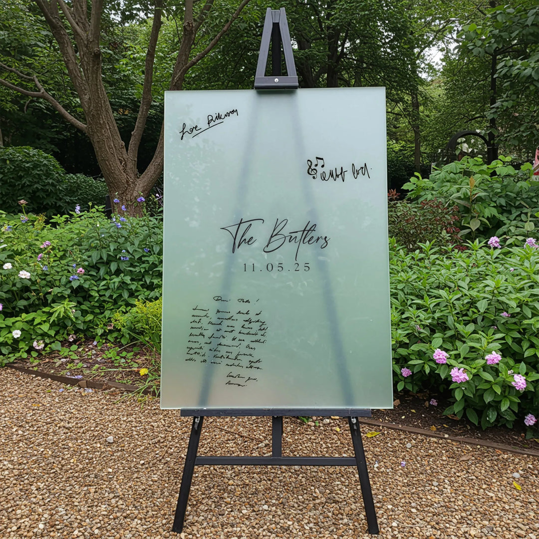 Frosted glass wedding guest book sign on black easel with The Butlers 11.05.25 in garden