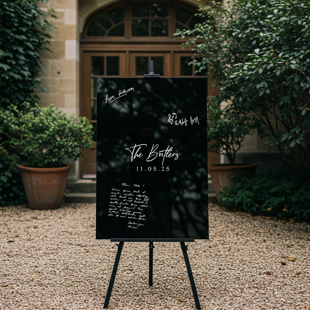 Elegant black wedding guest book sign with white calligraphy, The Butlers 11.05.25, displayed outdoors on an easel