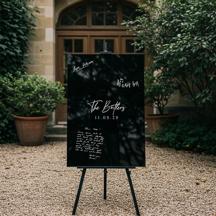 Elegant black wedding guest book sign with white calligraphy, The Butlers 11.05.25, displayed outdoors on an easel