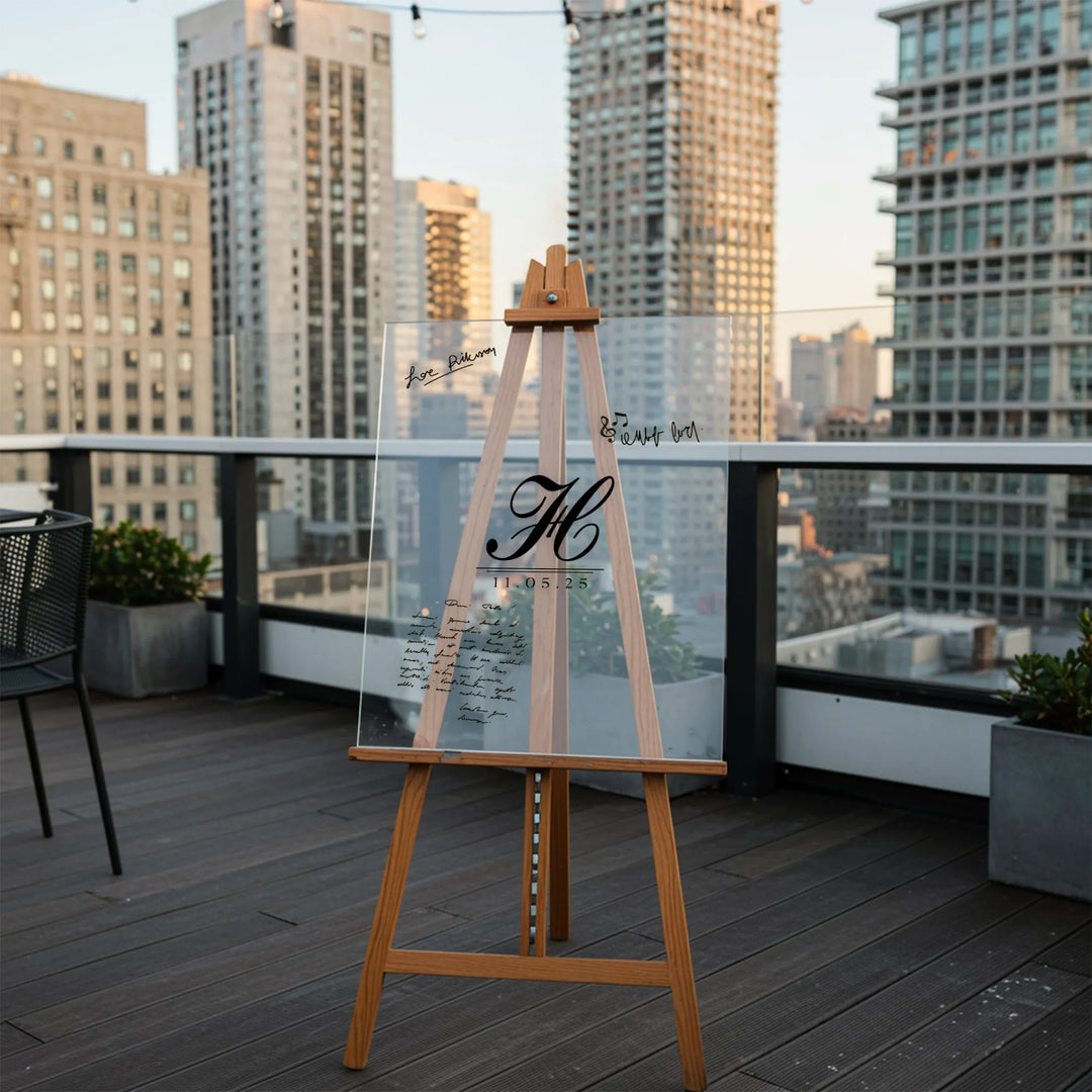 Clear acrylic wedding guest book sign with monogram on wooden easel on city rooftop
