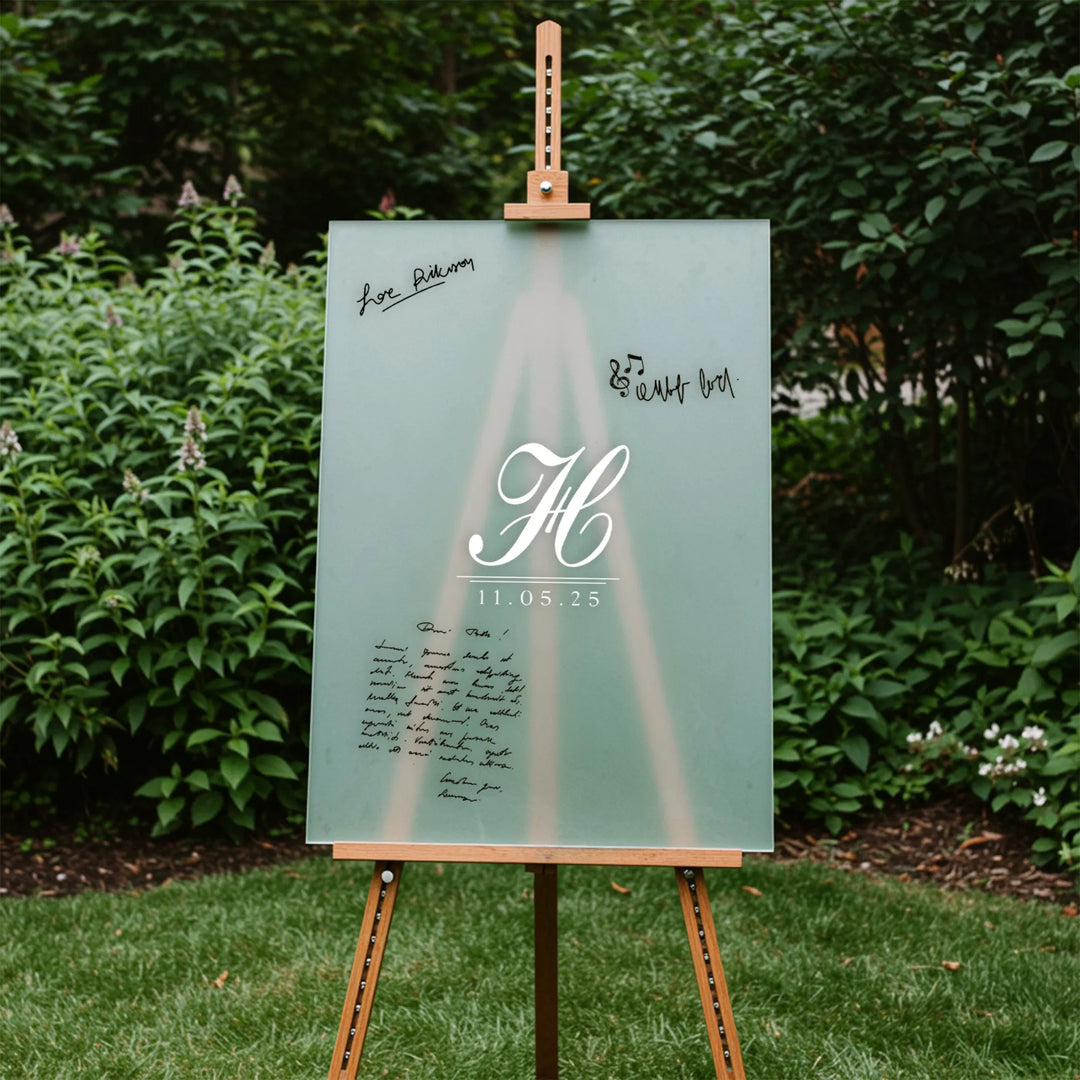 Frosted glass wedding guest book sign with monogram and date on wooden easel in garden