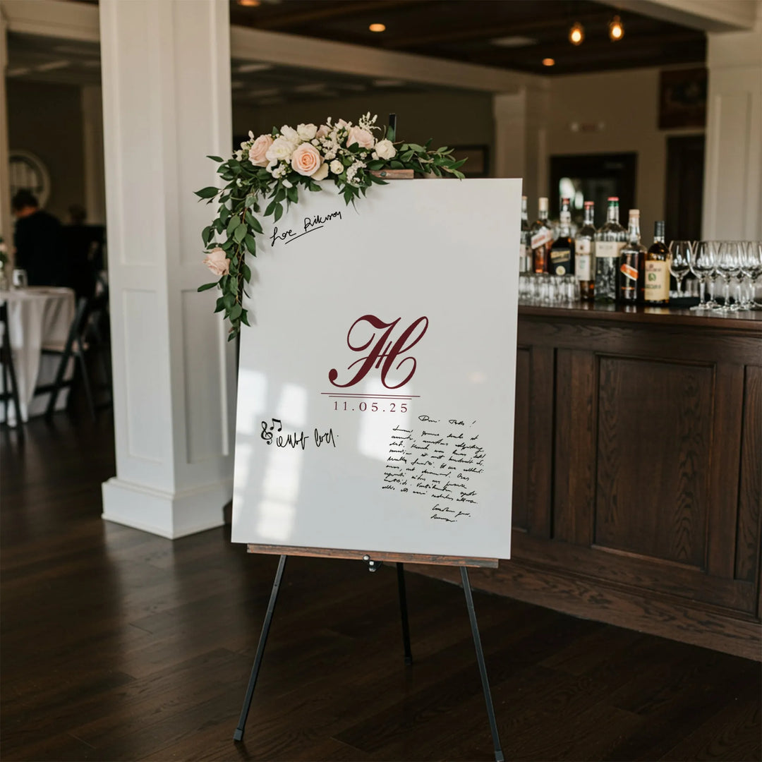 White wedding guest book sign with burgundy monogram and date, decorated with pink roses and greenery