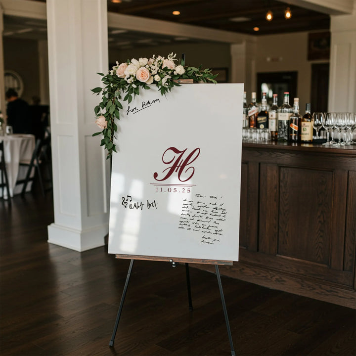 White wedding guest book sign with burgundy monogram and date, decorated with pink roses and greenery