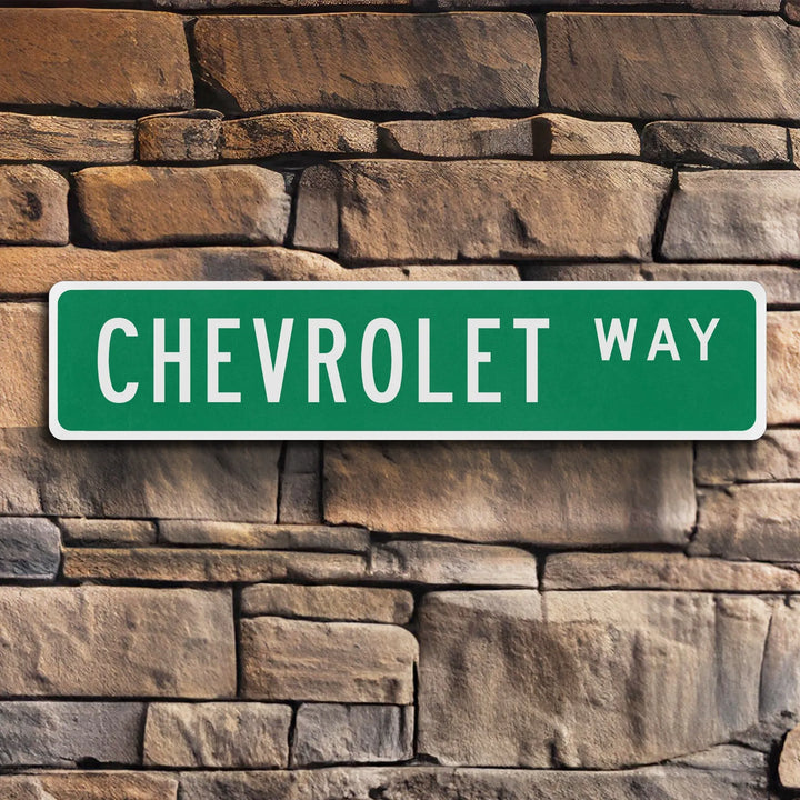 Green metal street sign with white border displaying Chevrolet Way text mounted on stone wall