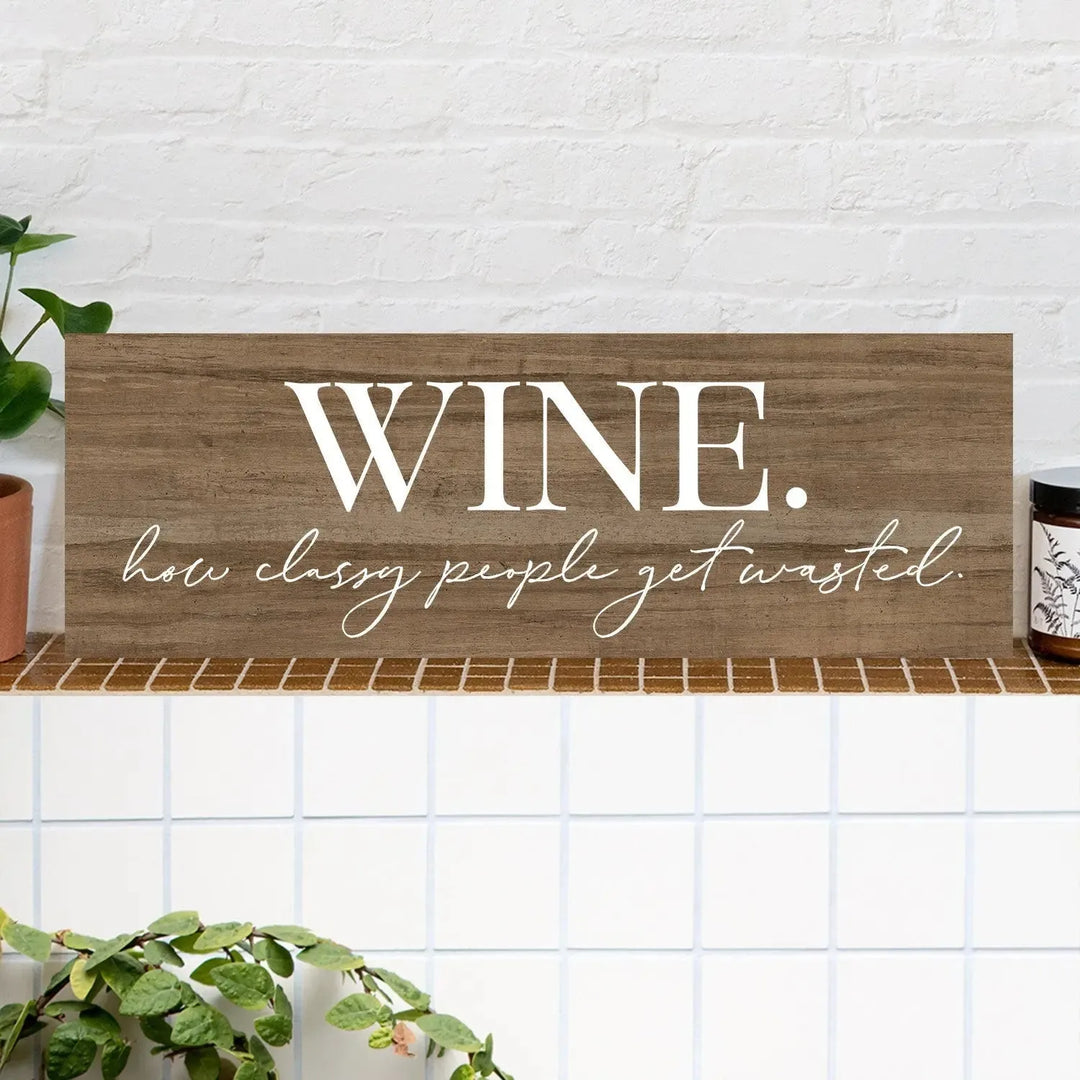 Rustic wood wine sign with 'WINE. how classy people get wasted.' on a tiled shelf.