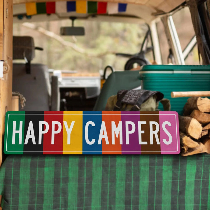 Colorful Happy Campers metal sign inside camper van with green cooler and firewood