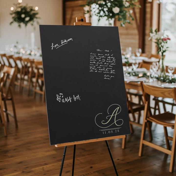 Black wedding guest book sign with monogram A and date 11.05.25 on wooden easel in decorated venue