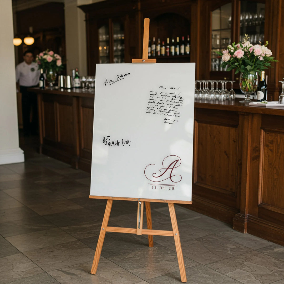 Wedding guest book sign with monogram A and date 11.05.25 on wooden easel in venue with bar and flowers